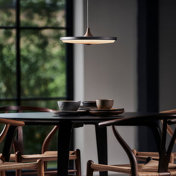 The Soleil LED pendant light from Le Klint above a dark, round dining table with wooden chairs